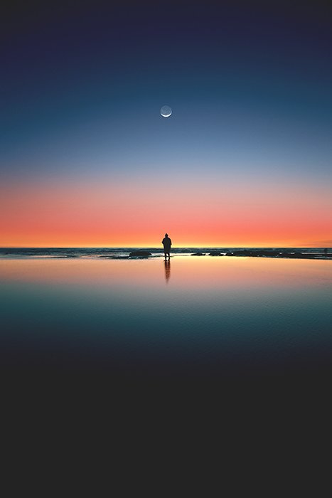 Потрясающий портрет одинокой фигуры на пляже под красочным закатом - симметрия в фотографии