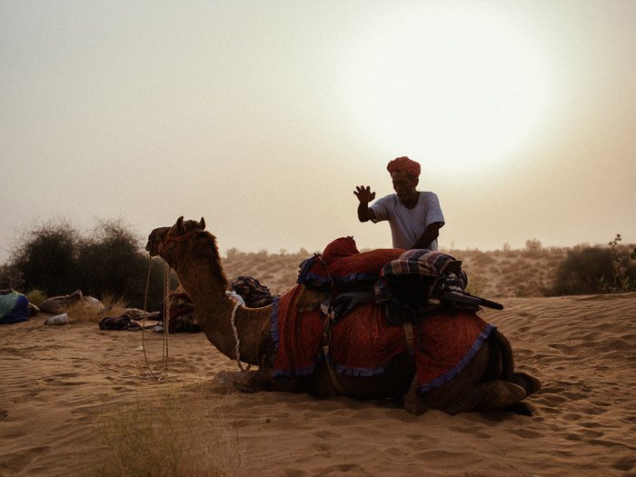 Портрет мужчины, стоящего у верблюда в пустыне, с красивой вспышкой объектива позади него