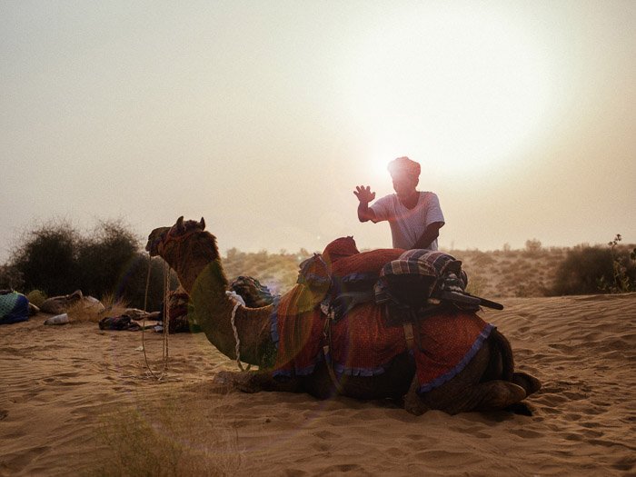 Портрет мужчины, стоящего у верблюда в пустыне, с красивым эффектом бликов позади него