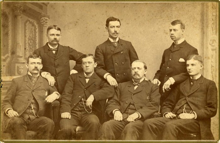 Старая групповая фотография семи мужчин, иллюстрирующая, почему люди не улыбаются на старых фотографиях