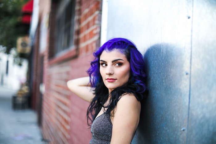 Портрет фотомодели с фиолетовыми волосами, позирующей у кирпичной стены
