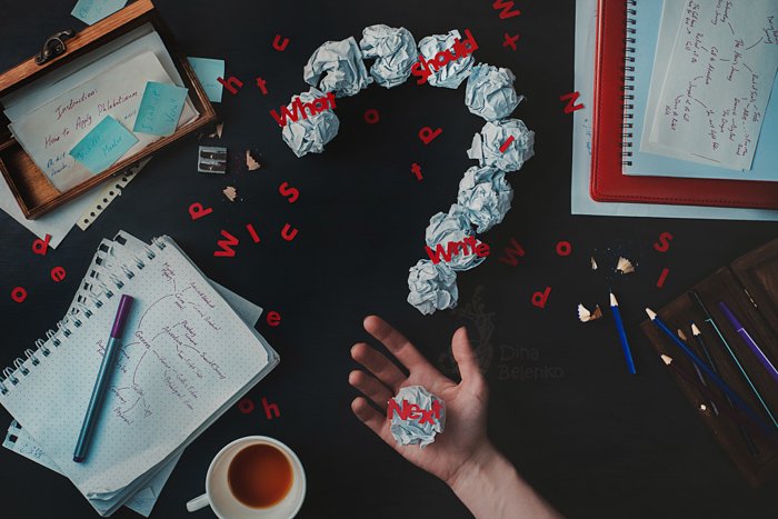A creative flat lay photo of the messy writing desk and a person holding a crumpled ball of paper with typography overlayed - creative still life photography composition