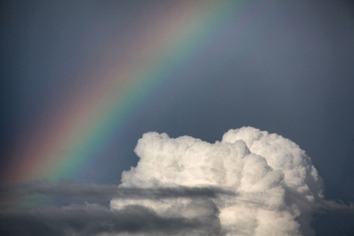 Потрясающая картина радуги рядом с белым пушистым облаком