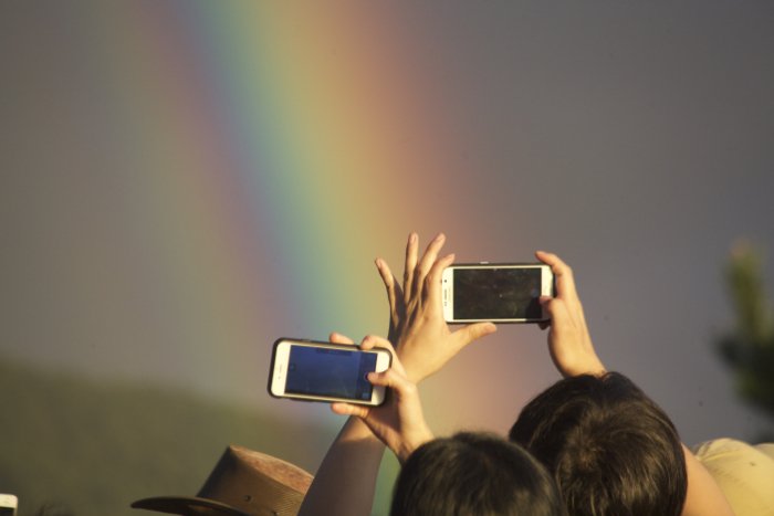 Два человека фотографируют радугу своими смартфонами