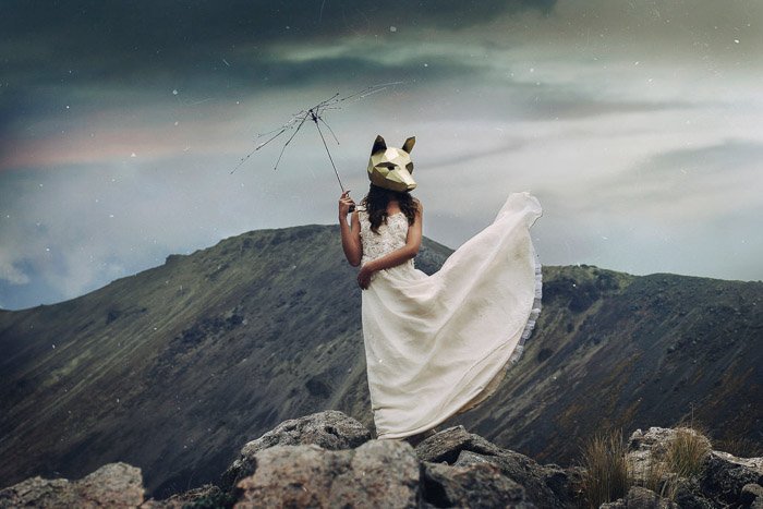 концептуальный портрет женщины-модели в маске волка, стоящей на фоне горного пейзажа