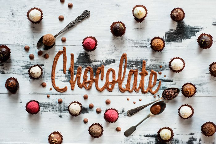 A creative flat lay ofchocolates and word 'chocolate' spelled with food typography hand painted background