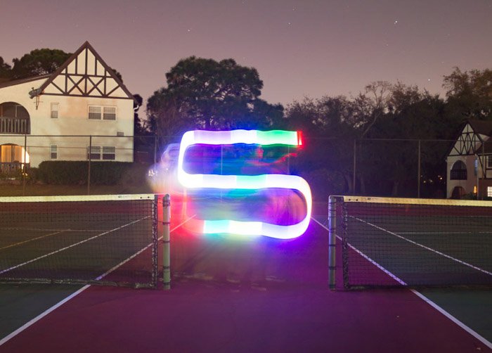 Красочная S-образная полоса светового рисунка, снятая ночью на теннисном корте с помощью светодиодных инструментов для рисования светом