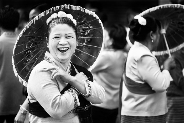 Черно-белый уличный портрет женщины с зонтиком, смеющейся с друзьями перед началом ежегодного парада цветов. Советы по нарративной фотографии