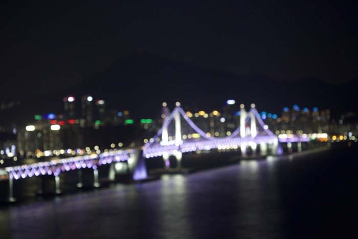 Размытое изображение освещенного моста над городской рекой ночью