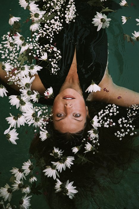 Мечтательная фотография женщины-модели, позирующей в воде в окружении белых цветов