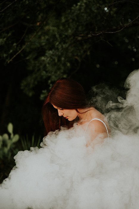 Dreamy portrait of the female model posing outdoors surrounded by smoke and dreamy background