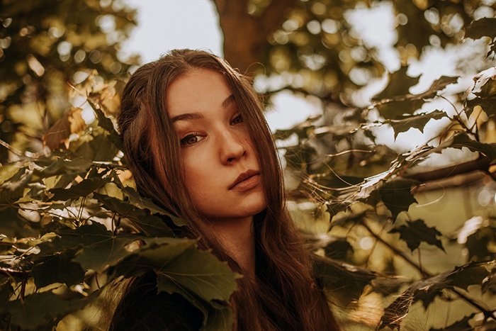 Dreamy photography shot of the female model posing outdoors among leaves - ethereal portraits