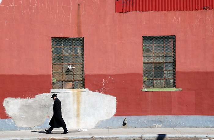 Художественная фотография человека, идущего по улице мимо красной стены