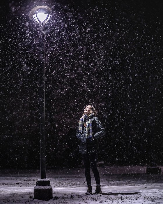 Атмосферный зимний портрет женской модели, позирующей под падающим снегом ночью