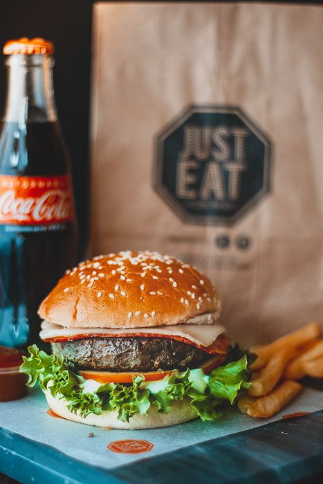 Вкусный гамбургер рядом с прохладительным напитком и бумажным пакетом для еды