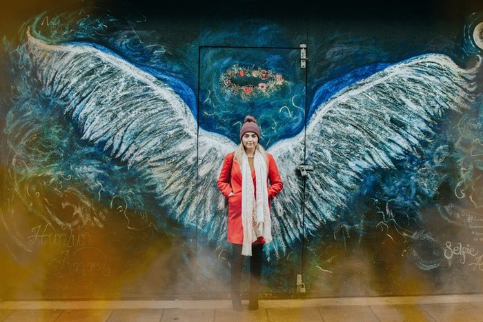 Женщина стоит перед стеной с нарисованными на ней крыльями ангела