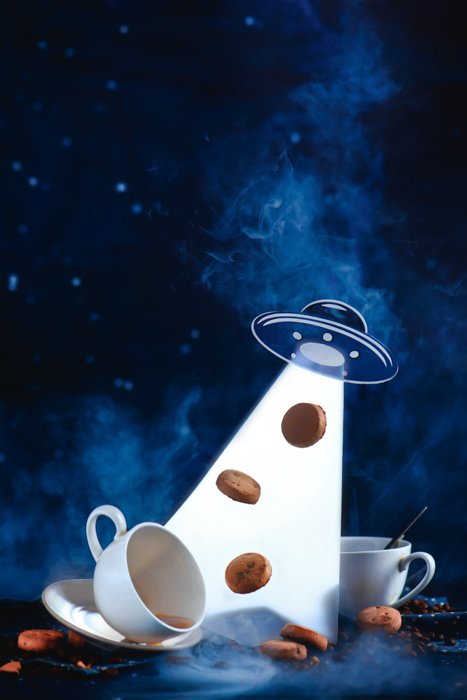 Натюрморт с космической тематикой, включающий кофейные чашки, сахар, печенье и летающую тарелку