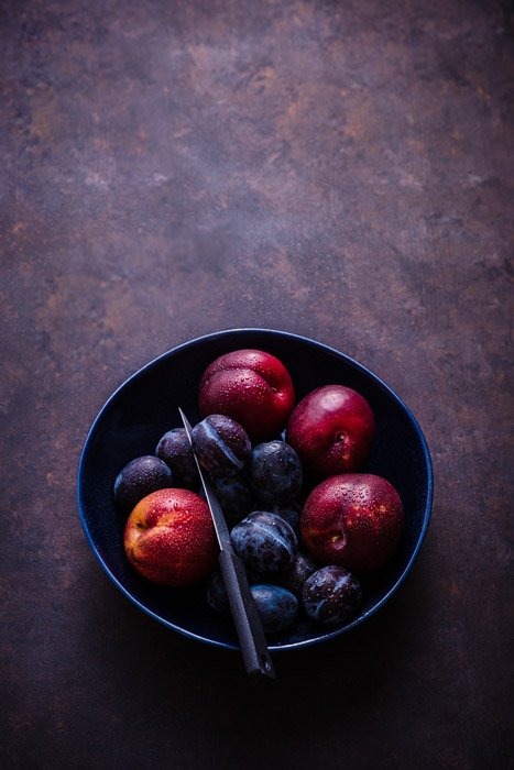 Темная и угрюмая фруктовая фотография сливы в миске