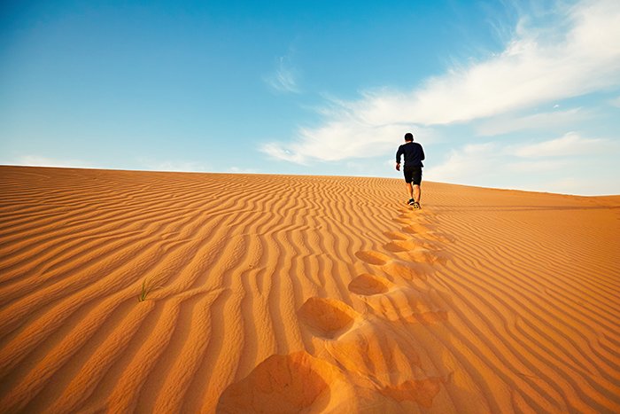 Молодой человек бежит к вершине дюны в пустыне.