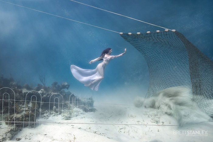 Dreamy underwater portrait of the female model swimming towards a net