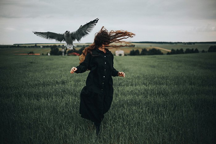 Концептуальный темный портрет женщины-модели, убегающей от птицы в поле - угрюмая фотография