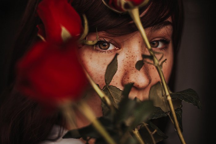 Атмосферный портрет крупным планом угрюмой женщины-модели с розами, покрывающими ее лицо - примеры темных портретов