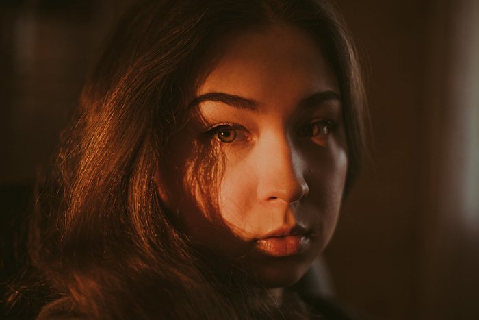 Атмосферный портрет угрюмой женщины-модели, смотрящей прямо в камеру при слабом освещении - примеры темных портретов