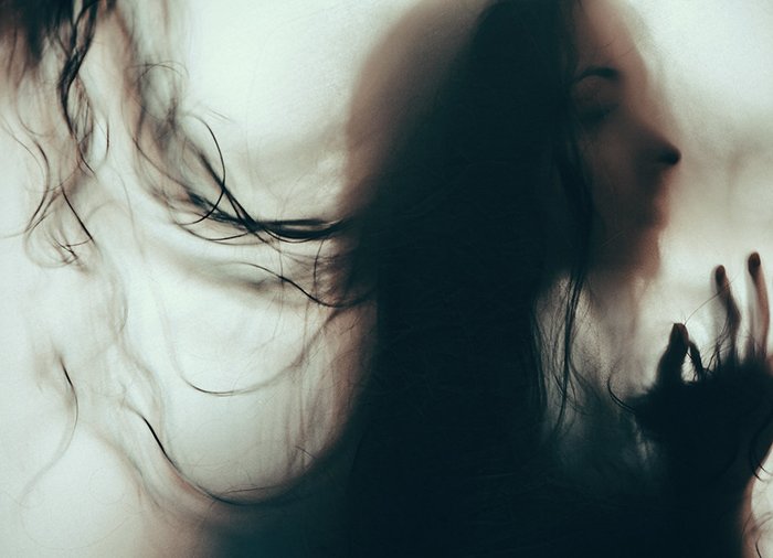 Атмосферный размытый портрет угрюмой женщины-модели с волосами, закрывающими лицо - примеры темных портретов