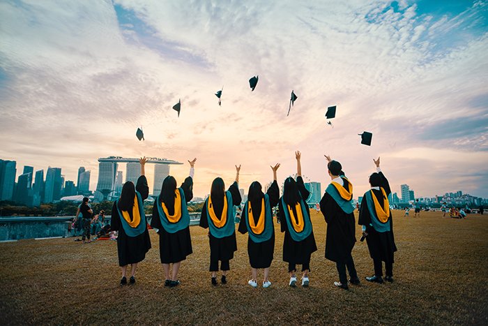 Группа выпускников подбрасывает шляпы в воздух - выпускная фотография