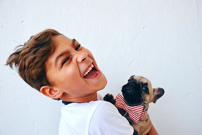 Веселый портрет смеющегося мальчика, держащего маленькую собачку - улыбающиеся люди