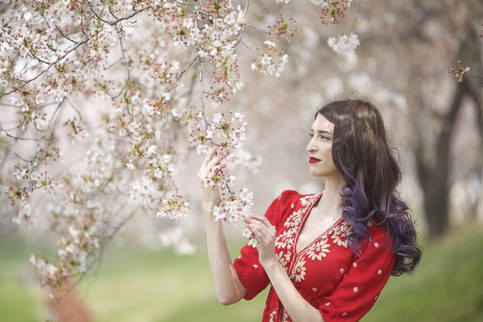 Женская модель в красном платье держит ветви цветущей сакуры