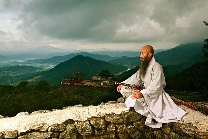 Монах, сидящий на стене и смотрящий вдаль, с прекрасным горным пейзажем позади него - правило пространства в фотографии