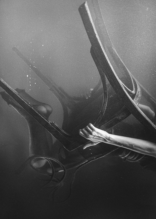 Художественная однотонная подводная фотография, изображающая человека на деревянном стуле, кувыркающегося дальше под водой