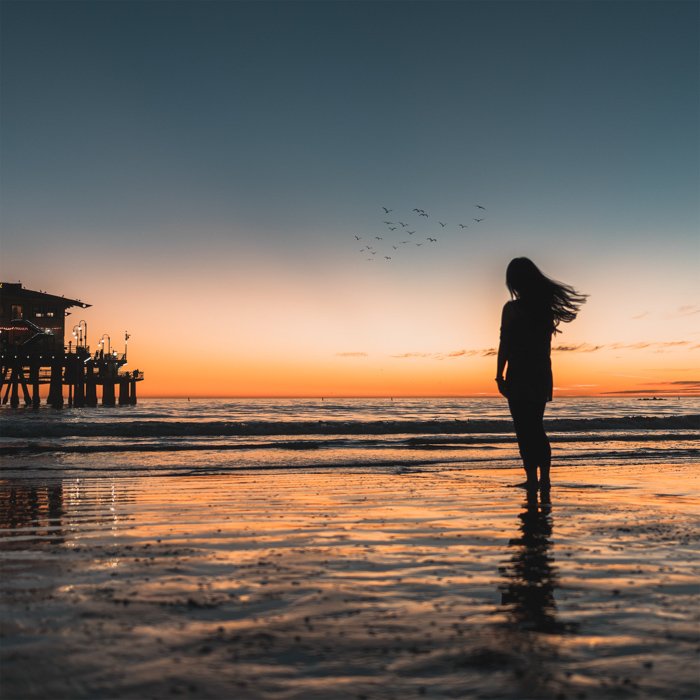 силуэт женщины-модели, стоящей на пляже на закате в летнее время
