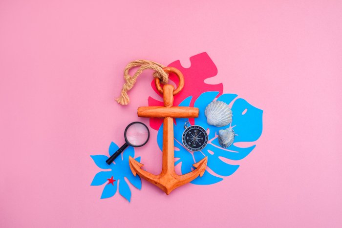 Summertime themed flat lay including an anchor and shells on pink background 