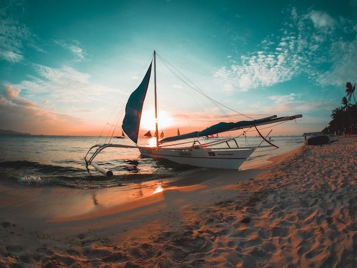 красивый снимок заката лодки на пляже с использованием тилово-оранжевой цветовой схемы