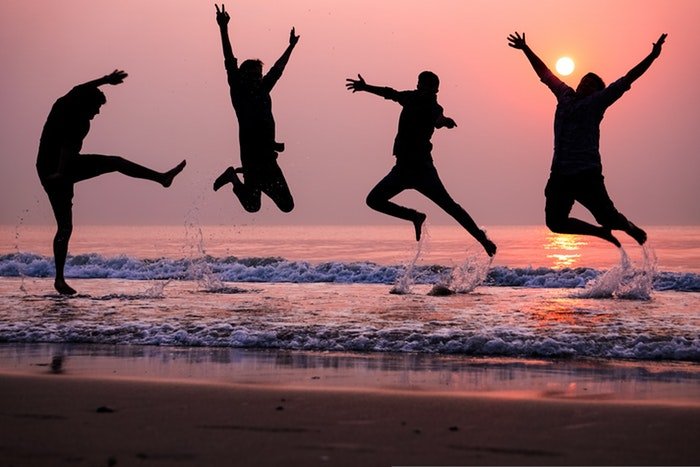 силуэты четырех людей, прыгающих от радости на пляже на закате, использование динамического диапазона в фотографии