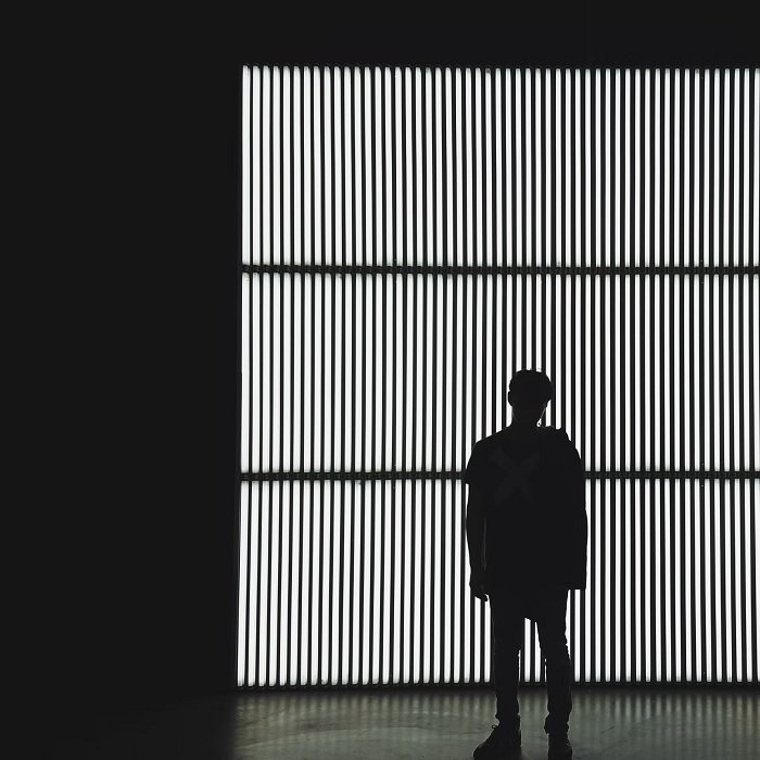 Черно-белая фотография мужчины, стоящего перед решетчатым окном