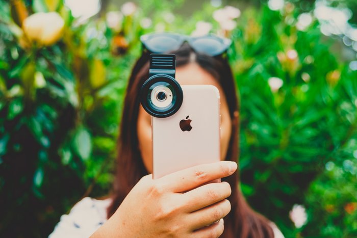 Фотография девушки, держащей iPhone перед лицом, чтобы сделать фото