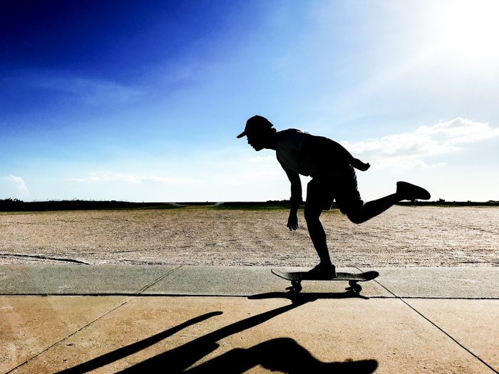 Фотография скейтбордиста в движении на фоне голубого неба