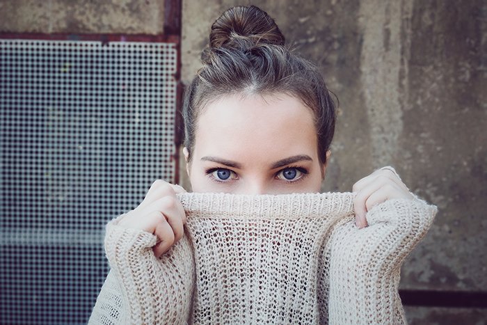 Портретная фотография женщины с голубыми глазами, натягивающей свитер перед ртом