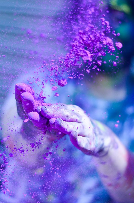Фотография крупным планом пары рук, бросающих порошок фиолетового цвета