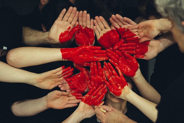 Фотография многих пар рук, окрашенных в красный цвет и образующих форму сердца