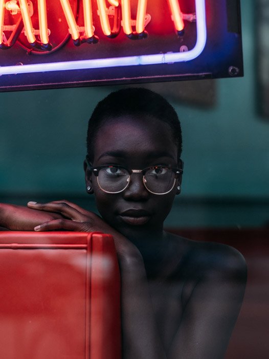 Портретная фотография женщины в очках, сидящей на красном диване за окном ресторана
