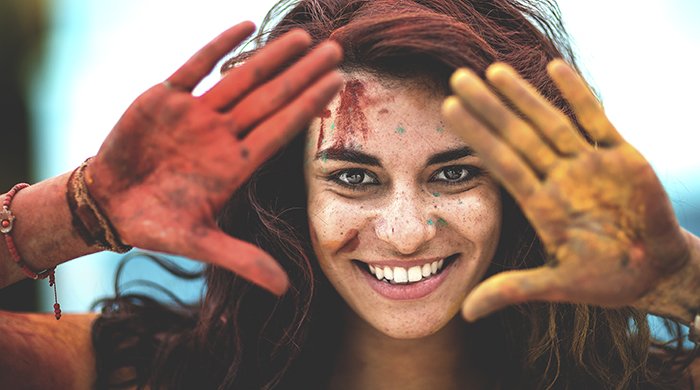 Молодая женщина держит руки, покрытые краской, вверх, чтобы обрамить лицо.