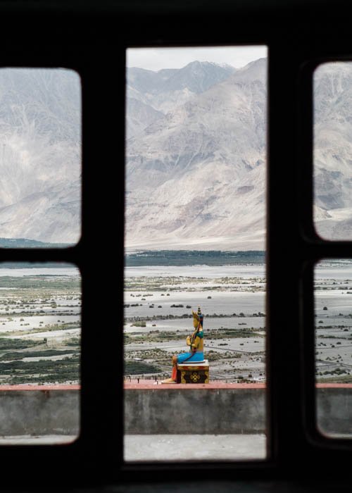 Фотография буддийской статуи, снятая из окна с горами на заднем плане