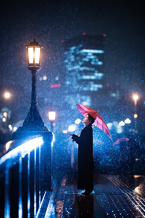 Фотография женщины, стоящей под зонтом на снегу с синими огнями на заднем плане