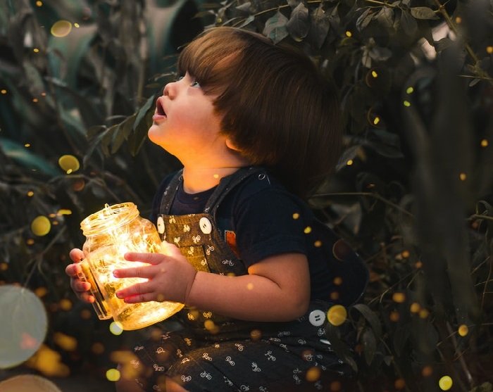 Child holding jar with fairy lights captured with bokeh photography effect 