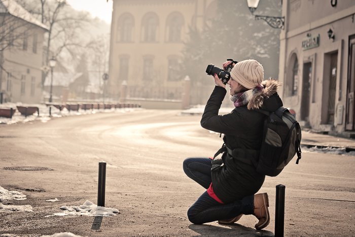 женщина-фотограф снимает уличную сцену на зеркальный фотоаппарат