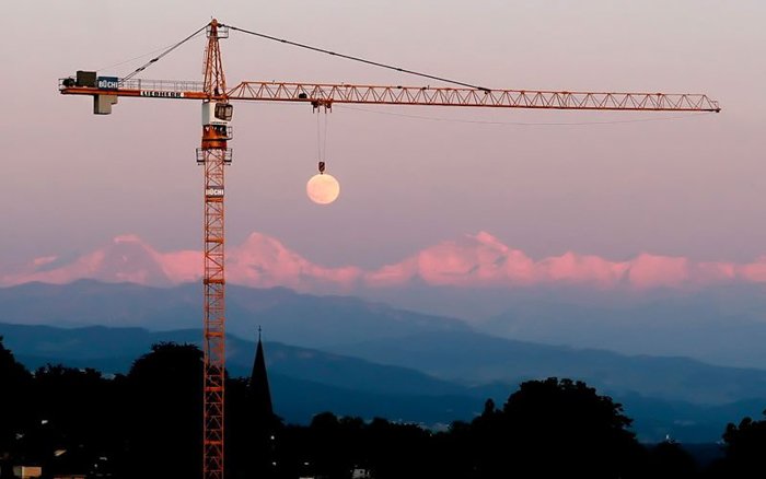 Фотография крана, держащего луну на заднем плане